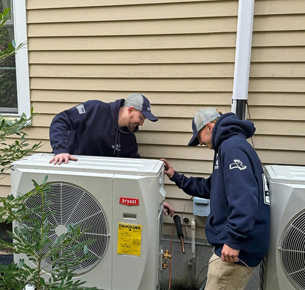 Smiling HVAC technician in uniform standing confidently with crossed arms next to a newly installed wall-mounted air conditioning unit. 