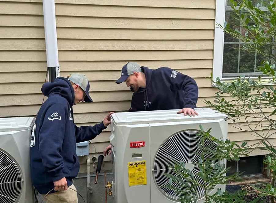 Female technician in a navy blue uniform inspecting or cleaning a wall-mounted air conditioning unit.