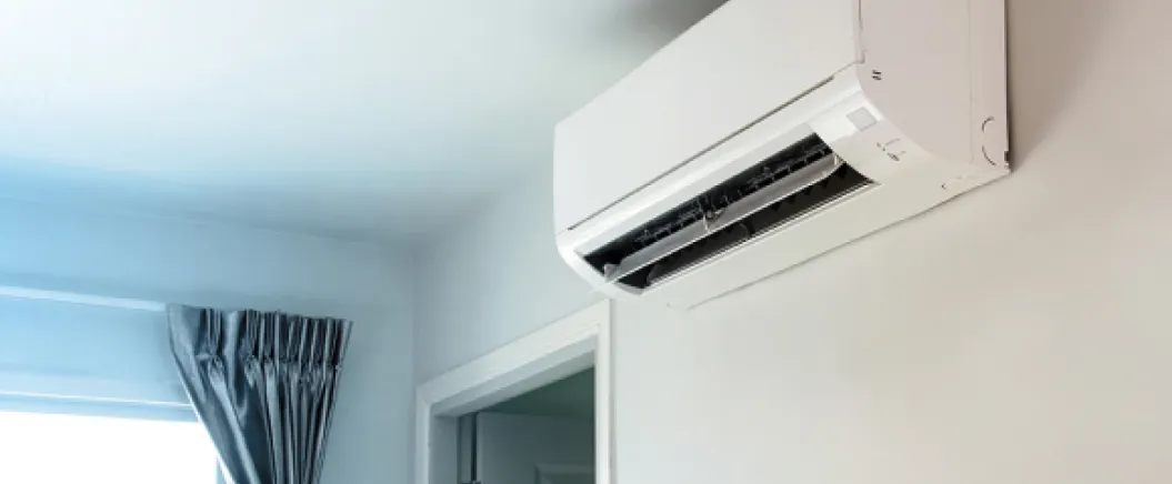 Wall-mounted split air conditioning unit installed in a modern room with a window and curtains.