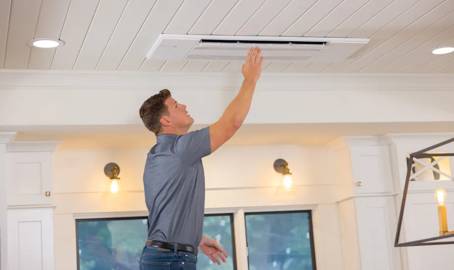 Technician adjusting a ceiling-mounted air conditioning unit in a well-lit interior space.